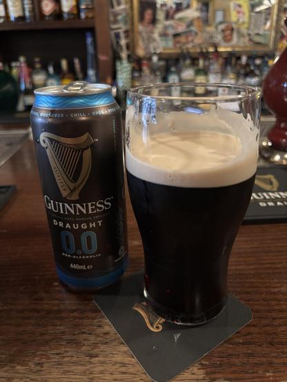 Glass of Guinness Zero on a pub counter, next to the empty can.