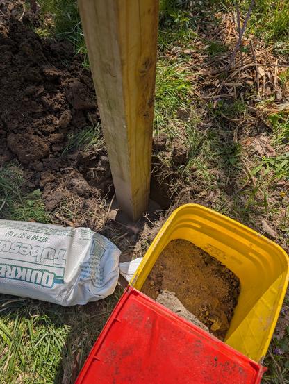 Photo of post in hole, bag of sand, and bucket of wood ash.