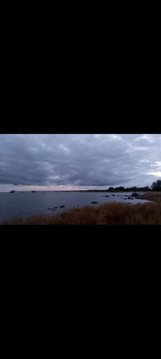 In the half-light, you can see the beach and the ocean, the sky is cloudy and where the ocean and sky meet you can see just a tiny bit of the sun.