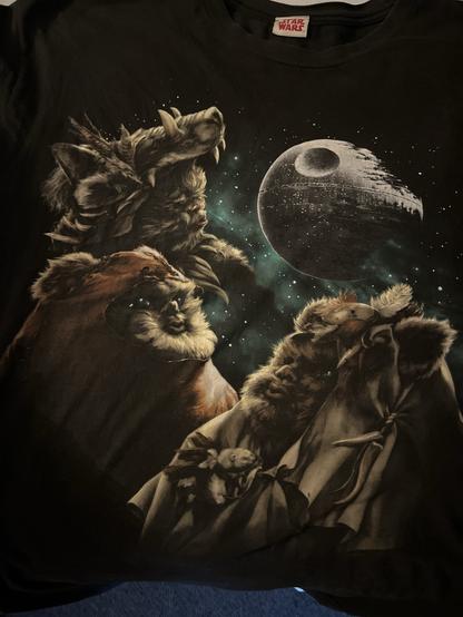 3 Ewoks howling at a blown out death star. Ewoks are mythical furry forest creatures. The Death Star is a gray and white orb.