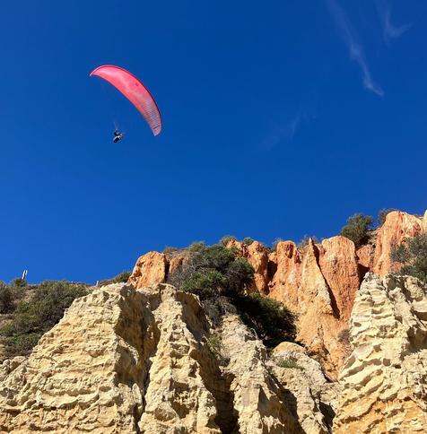 a paraglider glides above some steep cliffs