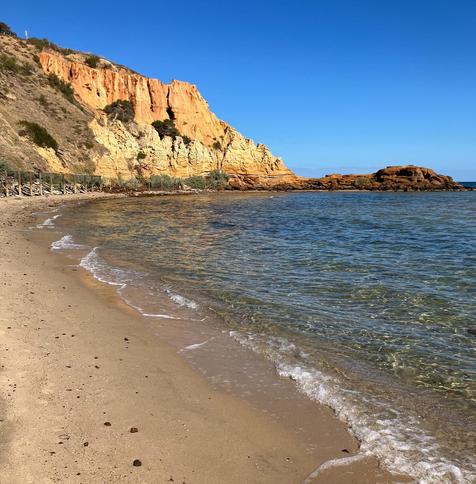 a beach with blue water and dramatic cliffs in the background