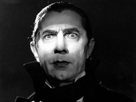 A black and white image of a man with pale skin and dark lips, hair, and eyebrows. Light is focused on his eyes, which gaze intensely into the camera. This is Count Dracula, the immortal vampire, and he is ready to hypnotize you, the viewer.