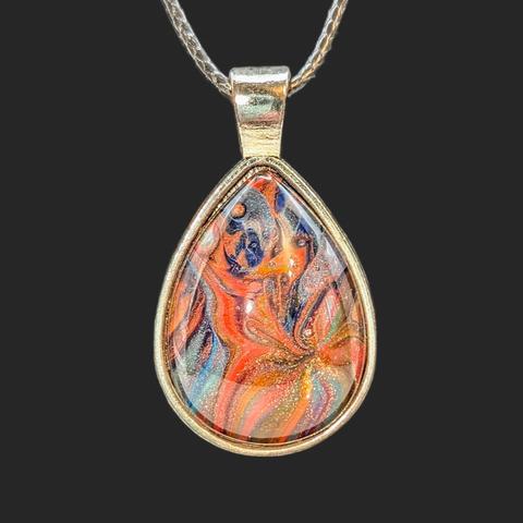 A close-up of a teardrop-shaped pendant. The setting is silver and the design is primarily orange and ultramarine blue.
