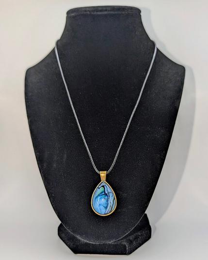 A teardrop-shaped pendant necklace displayed on a black jewelry mannequin. The setting is bronze and the design is primarily light blue.