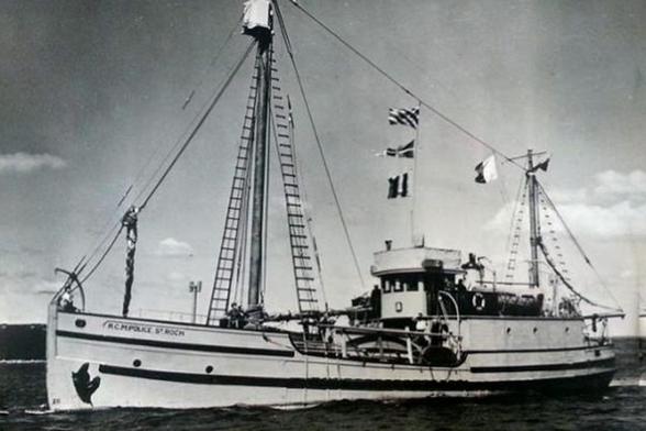 A vintage black and white photograph of the RCMPV St. Roch, a Royal Canadian Mounted Police schooner preserved at the Vancouver Maritime Museum. The ship is shown sailing on calm water with tall masts displaying flags, and its hull bears the inscription 'RCMP POLICE ST. ROCH'. This vessel holds historical significance as the first to circumnavigate North America and complete the Northwest Passage from west to east.