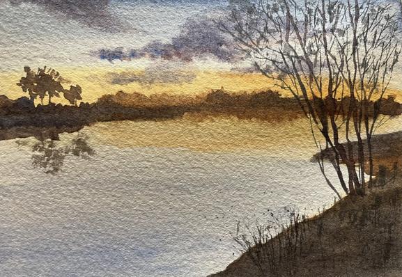 A quiet river stretches across the scene, reflecting a cluster of trees on the left and bare branches on the right, with soft, textured clouds drifting above a distant, low horizon.