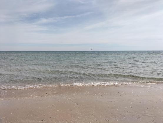 Beach with wet sand in the foreground and gentle wavelets, clear horizon with wispy cloud