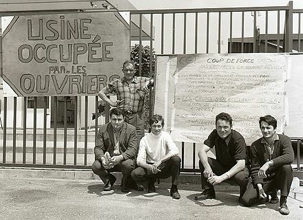 Strikers in Southern France, crouching with a sign reading "Factory Occupied by the Workers." Behind them is a list of demands, June 1968. By BeenAroundAWhile at en.wikipedia, CC BY-SA 3.0, https://commons.wikimedia.org/w/index.php?curid=47397033