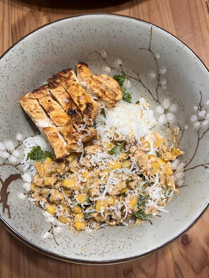 Photo of a bowl full of rice with cilantro, topped with grilled chicken slices and the corn/cream/cheese mixture.