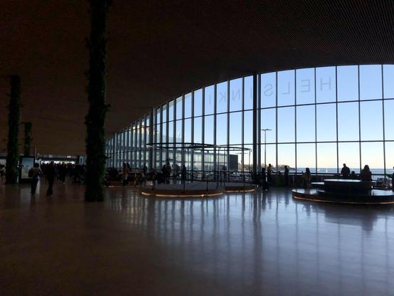 View to the ferry terminal with huge windows, giving out to the sea. People slowly wandering towards check in gates on left.