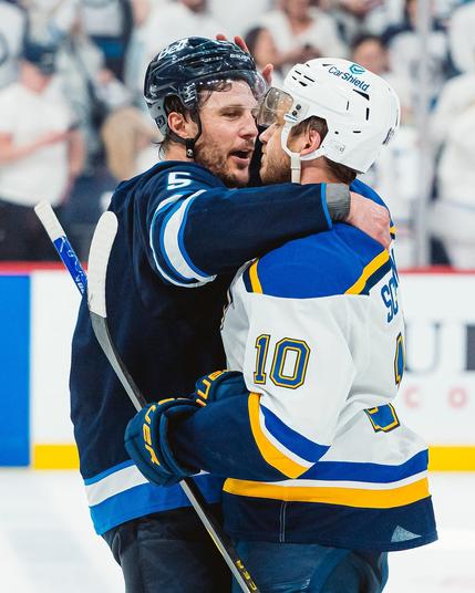Photo of Brayden Schenn in a St. Louis Blues away uniform hugging Luke Schenn in a Winnipeg Jets home uniform