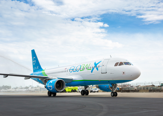 An aircraft with the livery of "GLOBAL X" is taxiing on an airport runway, surrounded by a partly cloudy sky. In the background, there is an airport fire truck and other vehicles.