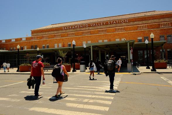 People are walking toward the Sacramento Valley Station, a brick building with large windows and a sign on top.