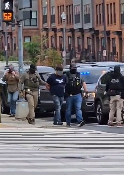Masked people in DC, one has a shirt that says Police, the others are unknown because there's no indication of who they are, & one has a person handcuffed that he's escorting.