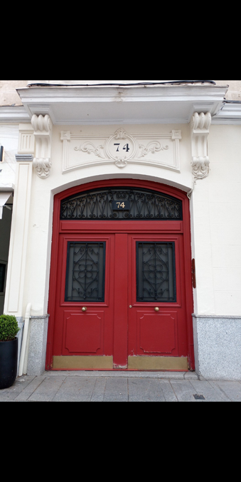 A wide set of double doors that are a bold red colour with black decorative metal panels and glass behind them. They bear the number 74.
