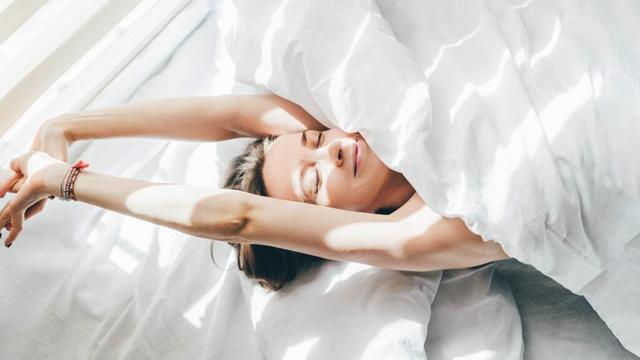 A photograph of a woman waking up and stretching in bed.