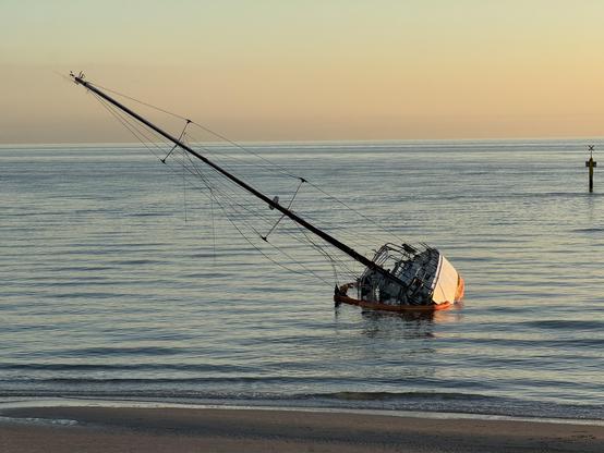 Photo of a yacht that has run aground in shallow water. It is tilted at 45 degrees and is partially submerged.