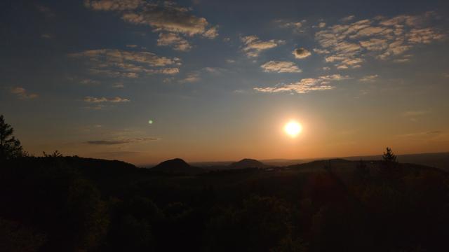 View from mountain over some other small mountains with the sun some time before sunset