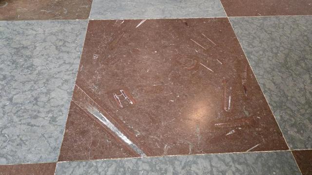 A photo of a marble floor with red and white slabs. The red slabs are full of long striped cones - belemite fossils