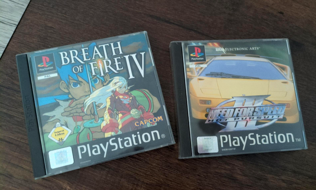 PAL PS1 versions of Breath of Fire IV and Need for Speed III next to each other on a wooden table.