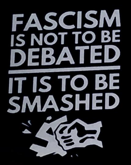 World War 2 propaganda poster; light grey text on a black background stating "Fascism is not to be debated - it is to be smashed". Below the text is a fist breaking a swastika.