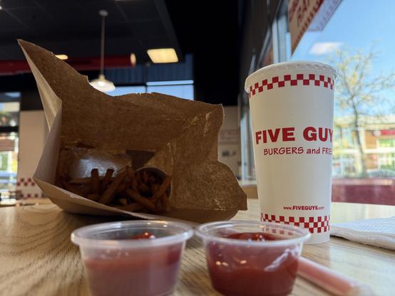 A bag of fries and a burger. A cup of Mello Yellow. Two tiny cups of ketchup.