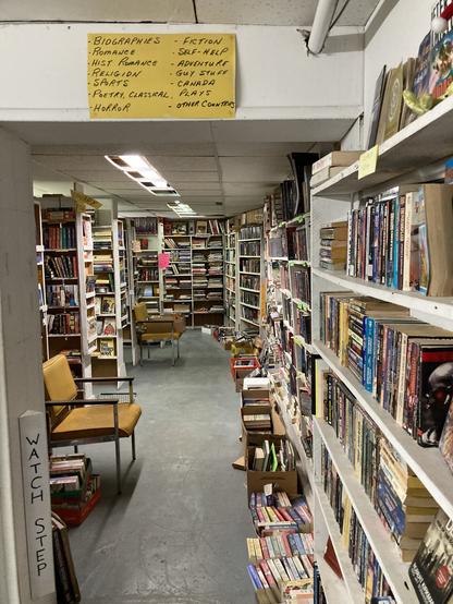 Endless rows of used books along a wall, snaking around a poorly lite basement bookstore. You see one of those old 1970s yellow office chairs in the distance.