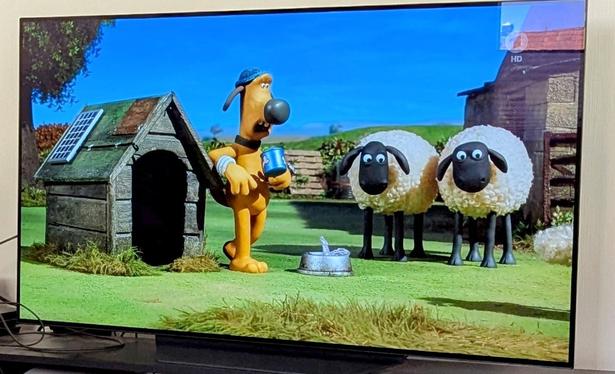 Eine Scene aus der Kinderserie Shawn das Schaf. Der Hofhund Bitzer steht vor seiner Hundehütte und trinkt Kaffee. Daneben zwei Schafe. Der Hofhund Bitzer hat ein kleines PV Modul auf seiner Hundehütte.