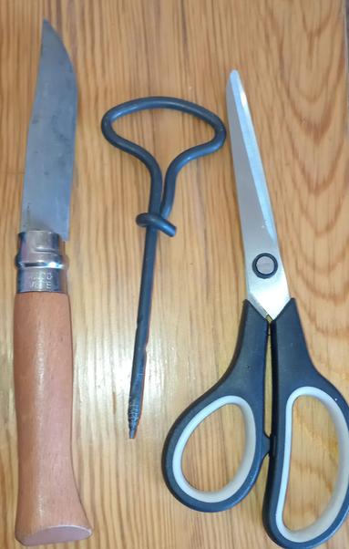 photo of three tools lying on a wooden table: a pocket knife with wooden handke, an awl and kitchen scissors