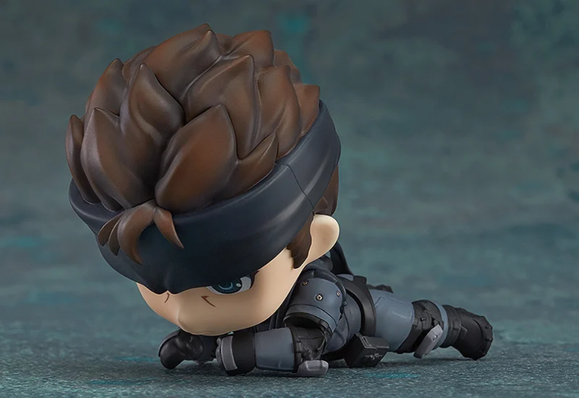 a photo of the figure, it is snake from metal gear, wearing his tactical garb , his head is larger and his features are a cute anime style, he is doing an army crawl in the photo