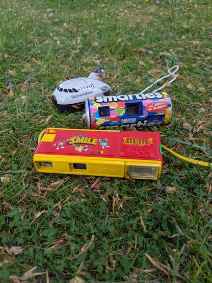 three cameras. one shaped like a plane. one shaped like a Smarties tube. one with m and m's branding