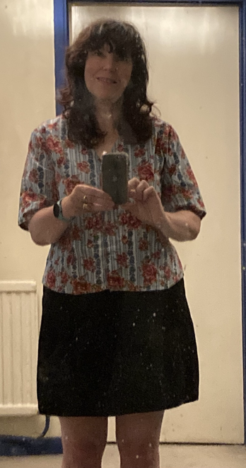 Middle aged woman wearing an oversized floral print V neck shirt and an A line above the knee skirt