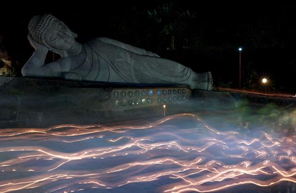 Devotees carry candles and walk around a Buddha statue on the eve of Vesak Day (a long exposure photo).