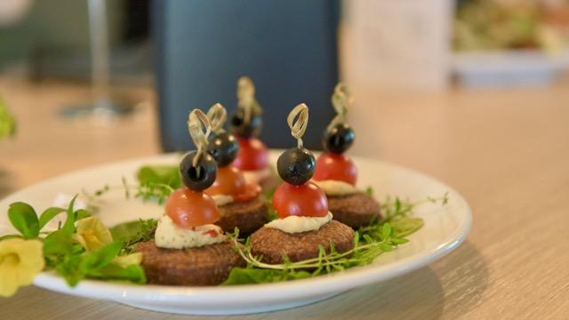 Cute little falafel with a cherry tomato and a black olive on top, staying within the limits of our corporate identity