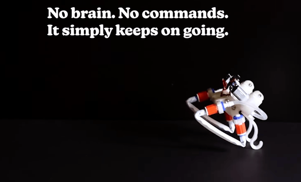 A small white soft robot with flexible tubular limbs and orange/red connection points is suspended against a black background.