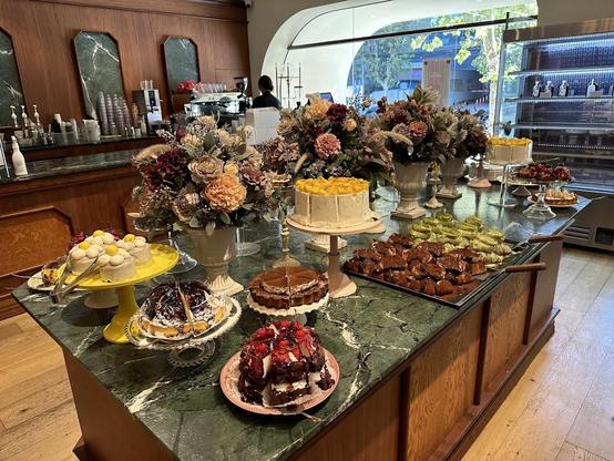 A display of cakes and pastries are arranged on a countertop with vases of flowers.