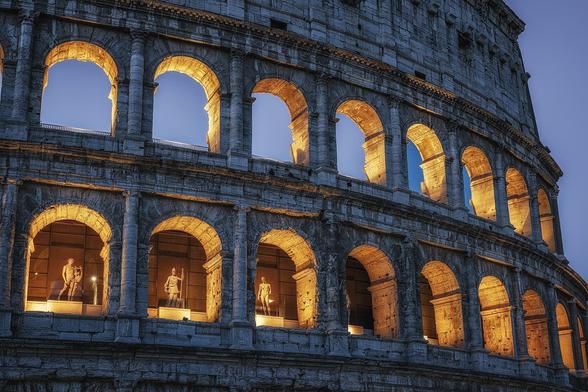 A blue hour photograph of the Colosseum in Rome Italy. The arches are illuminated from within creating a warm glow in the arches, while the external structure is cool in the morning light.