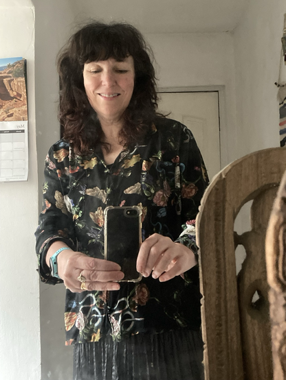 A middle aged woman wearing a loose fit shirt with three quarter length sleeves, black printed cotton lawn with butterflies, moths, snakes, beetles and flowers