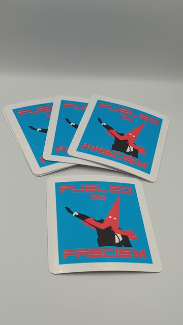 A large 4" square sticker reading in the Tesla motors font: Fueled by Fascism. In the centre is a twist one elon musk throwing a seig hiel on live TV. He's wearing an inverted Tesla T logo over his head like a hood. White eyehole cutouts make the sharp point of the logo look exactly like a KKK pointy hat for losers.