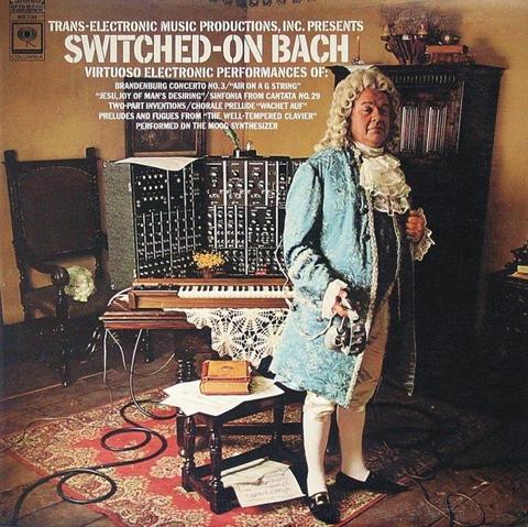 Album sleeve of SWITCHED-ON BACH by Wendy Carlos. Photo of an actor posing as Bach in modest room with dark wooden furniture, visible floorboards, and a patterned red rug. He is wearing a white curly period wig, along with light blue silk long embroidered jacket, dark blue waistcoat, white breeches and stocking, black leather pumps, and a frilled lace cravat. Subtly, he is holding a rather incongruous pair of headphones. Less subtle is the modern keyboard and modular Moog synthesizer on the table behind him. Title and cover text:

TRANS-ELECTRONIC MUSIC PRODUCTIONS, INC. PRESENTS SWITCHED-ON BACH, VIRTUOSO ELECTRONIC PERFORMANCES OF:
BRANDENBURG CONCERTO NO.3 / "AIR ON A G STRING" / "JESU,JOY OF MAN'S DESIRING"/ SINFONIA FROM CANTATA NO. 29 / TWO-PART INVENTIONS / CHORALE PRELUDE "WACHET AUF" / PRELUDES AND FUGUES FROM "THE WELL TEMPERED CLAVIER".
PERFORMED ON THE MOOG SYNTHESIZER.
