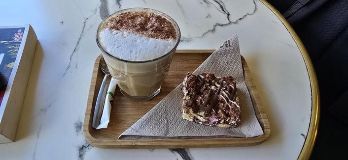 Coffee with foam and a pastry on a wooden tray on a white marble table.