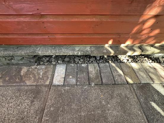 A detail of the edge of the floor of my wood store. Concrete flagstones are edged with paver bricks, which in turn are edged by pebbles.
