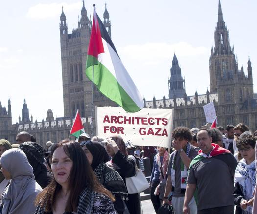 crowd of people with Palestinian flags and 'architects for Gaza' with the Parliament in the background