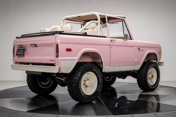 the vehicle photogpahed from behind in a three quarter view, it is pink with white accents, a white interior