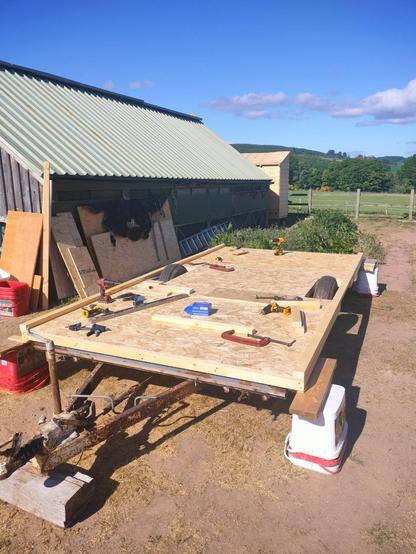 A two wheel chassis with a wooden base and wooden floorboards fitted. Woodworking tools are strewn across the completed flooring.