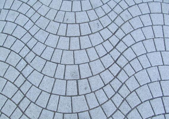 A photograph of grey street paving. It has a way pattern made of almost-rectangular blocks.
