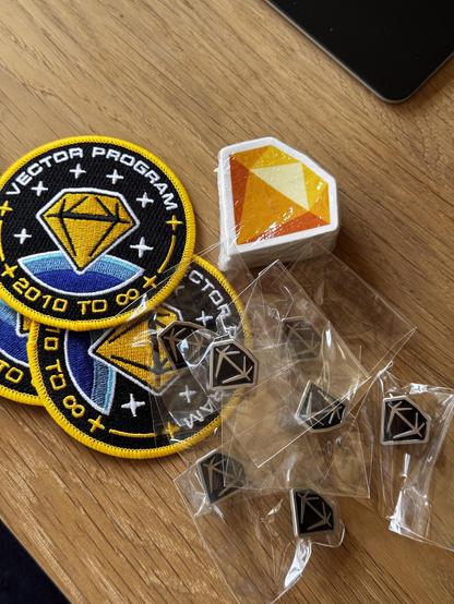 Picture of Sketch swag on a table: some of our exclusive Vector Program patches, the yellow Sketch gem sticker, and black metallic Sketch gem pins.