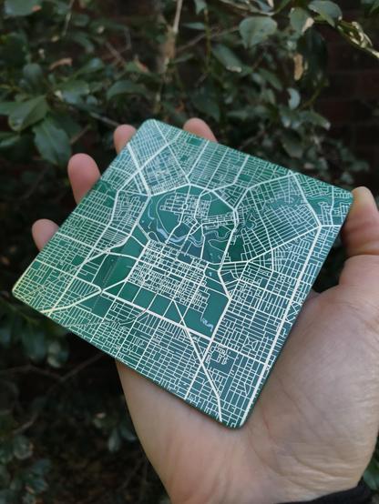 Photo of a coaster featuring a map of the city Adelaide. It's fabricated as a printed circuit board - green is the main background colour and the roads are a shiny gold colour.