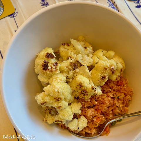In a white bowl, a large portion of oven baked cauliflower placed on a bed of red colored rice.
